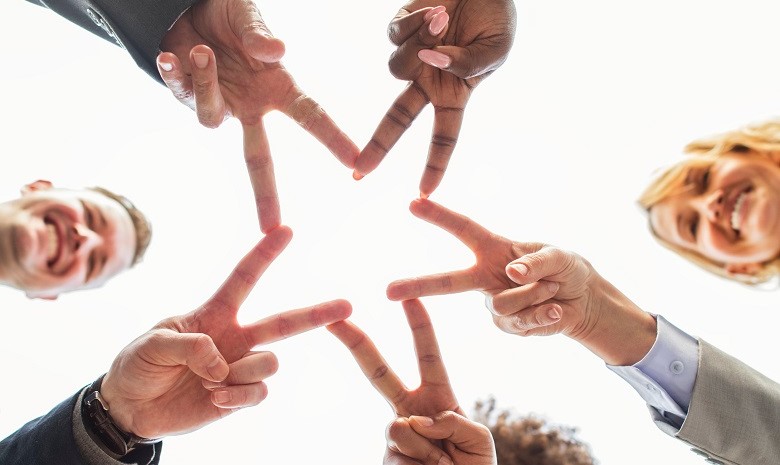 Eine Gruppe aus fünf Menschen formt mit ihren Fingern gemeinsam einen Stern, fotografiert von unten