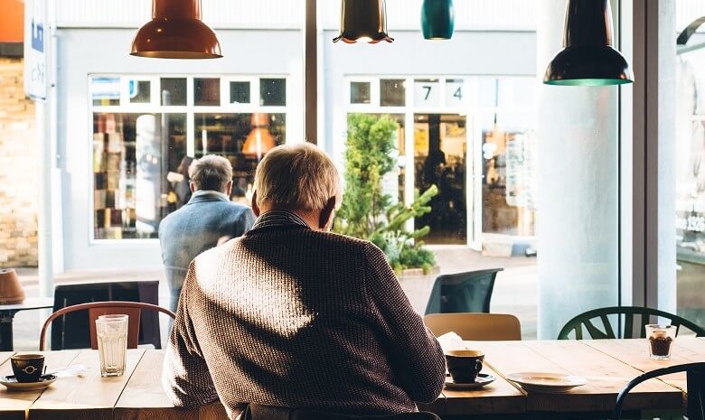 Krankengeld für Selbstständige Beitragsbild: Ein Rentner sitzt mit einer Tasse Kaffee in einem Café