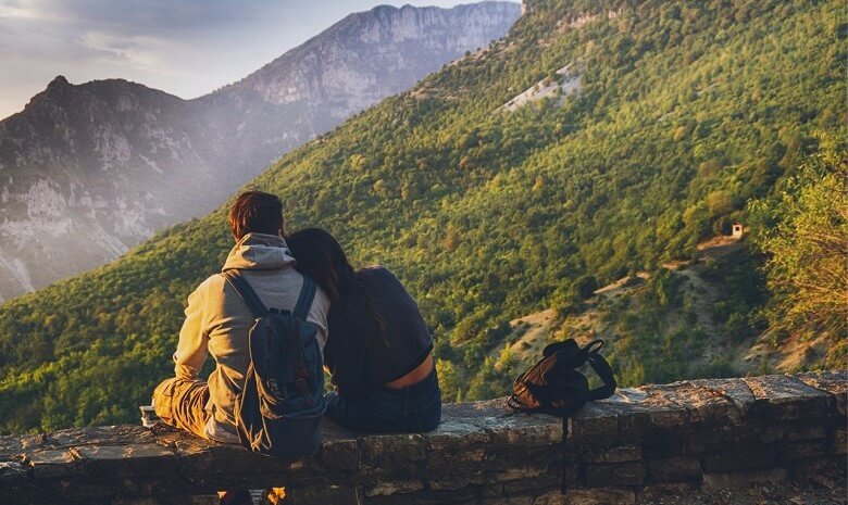 Tipps für Texter 2020 Beitragsbild 4: ein Paar in Wanderausrüstung sitzt auf einer Mauer mit Ausblick auf die Berge.