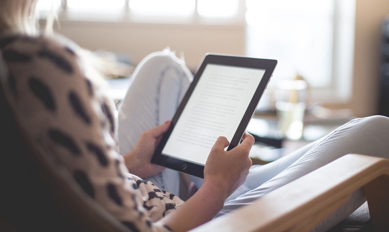 Blick über die Schulter einer jungen Frau auf ihr Tablet, das sie in der Hand hält, um zu lesen.