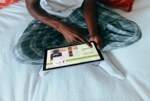 Mann sitzt mit iPad auf Bett